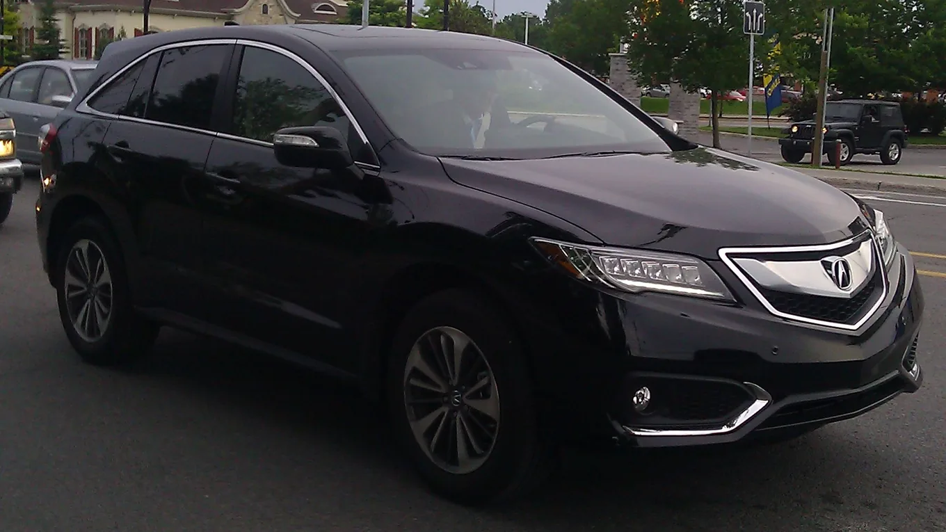 Black Acura RDX SUV on a street with its LED headlights lit, seen from the front right