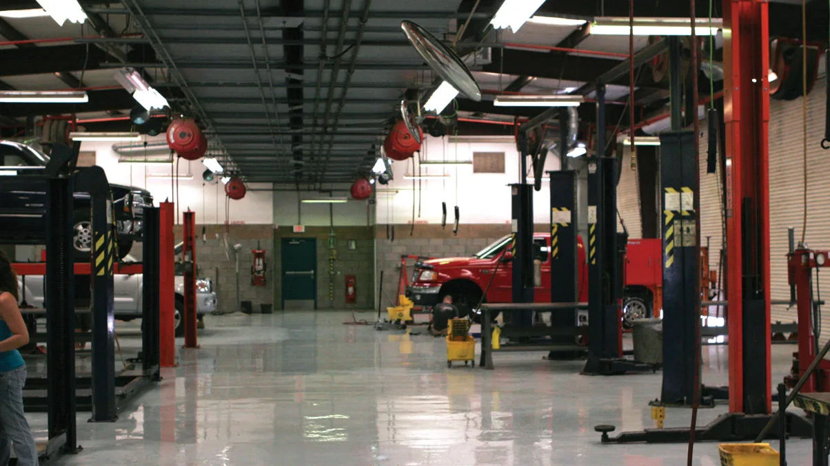 Interior of a large auto service center with hydraulic lifts, a red pickup in a service bay and air hose reels overhead