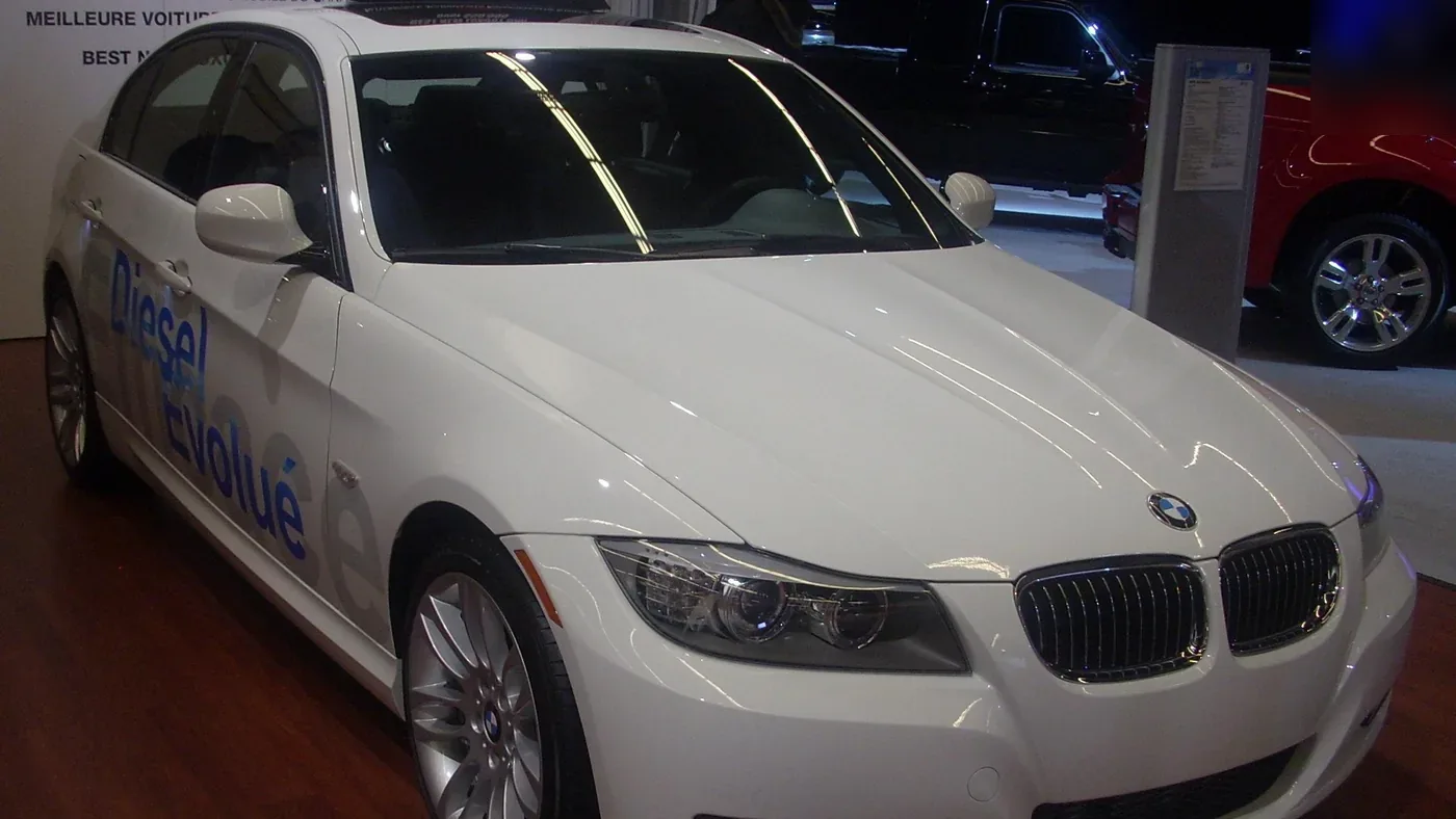 White 2010 BMW 3 Series sedan on display at an auto show, seen from the front right