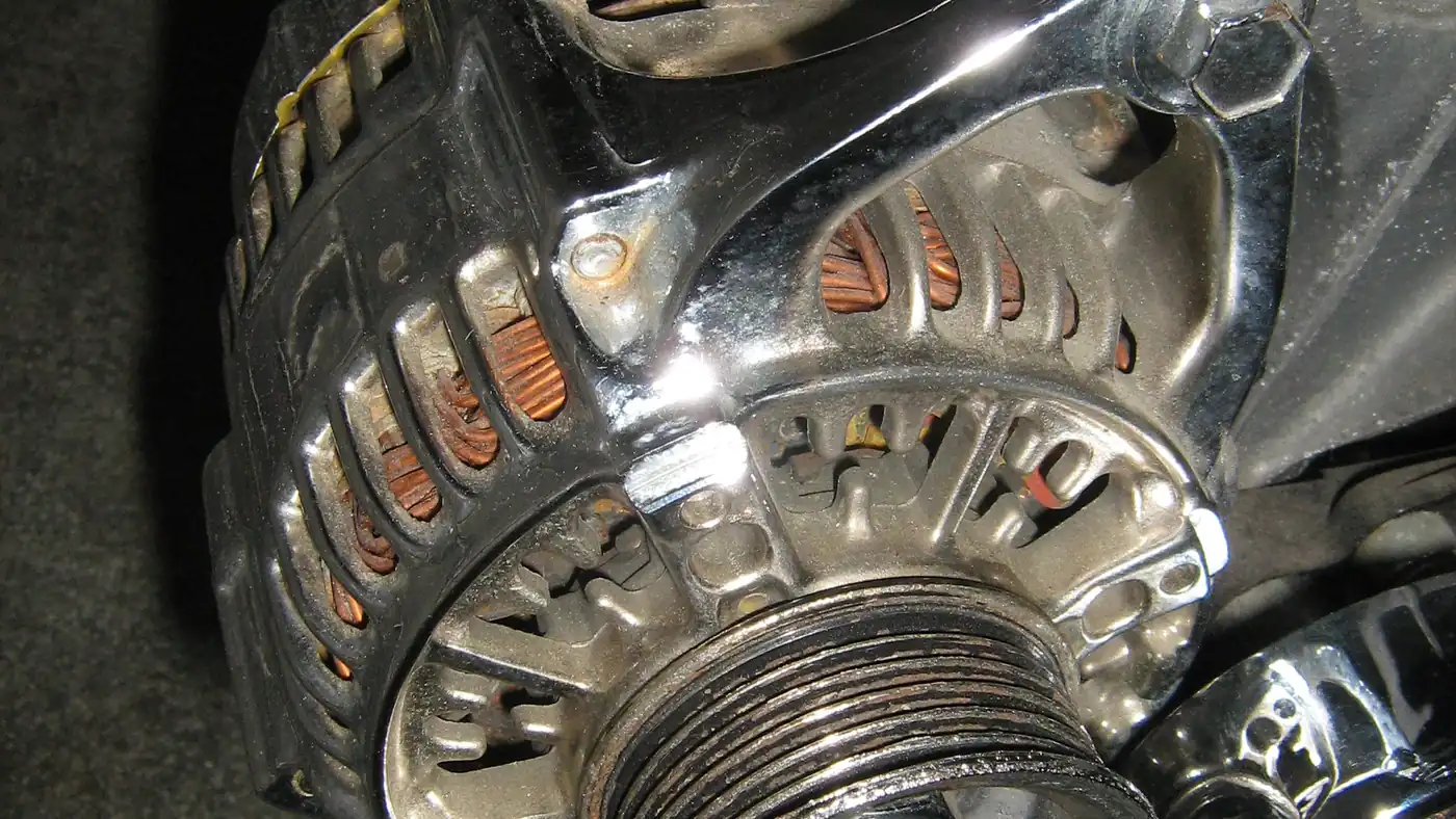 Close-up of a chrome-trimmed car alternator showing its copper windings and drive pulley