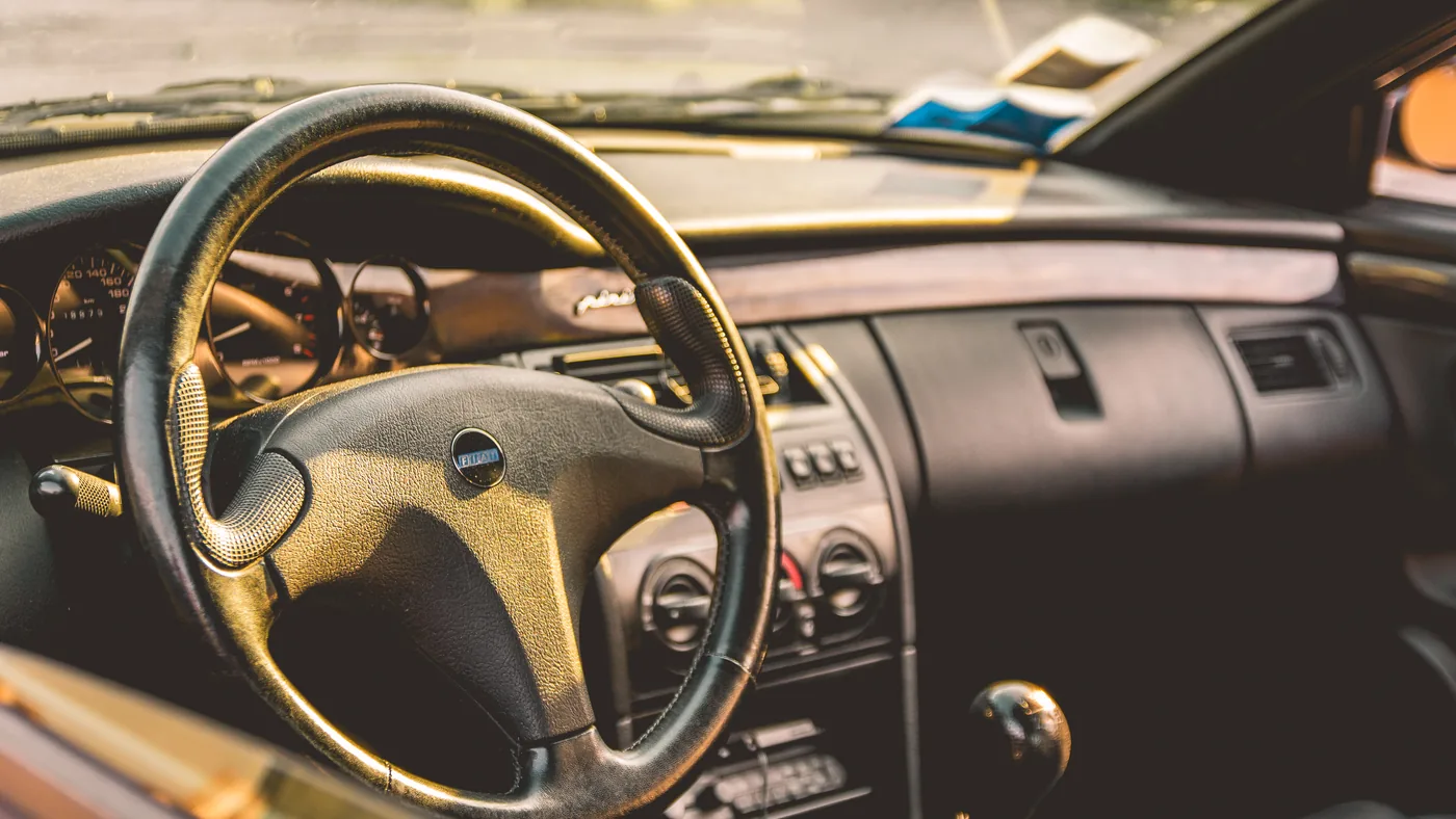 Sunlit interior of an older hatchback showing the steering wheel, analog gauges and a manual gear lever