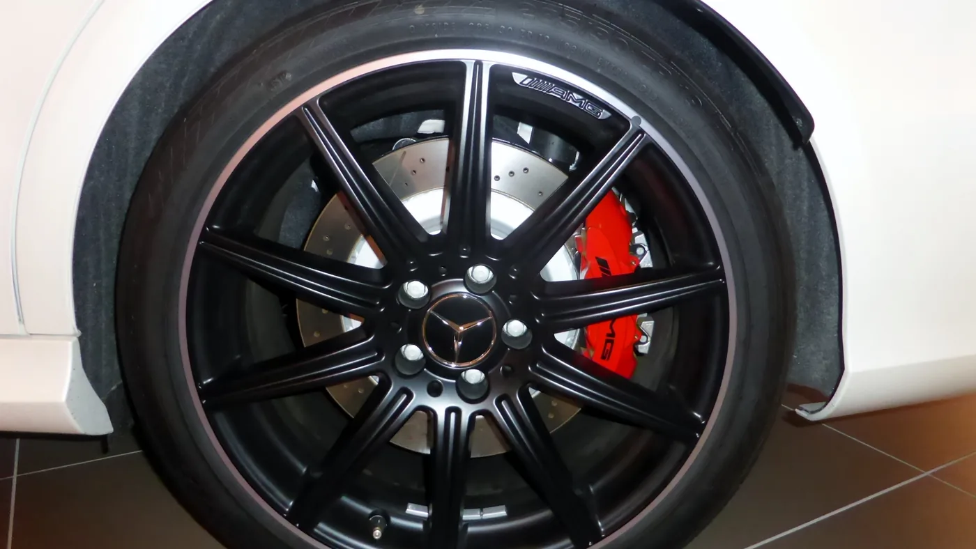 Close-up of a black alloy wheel showing a cross-drilled brake rotor and a red brake caliper behind the spokes