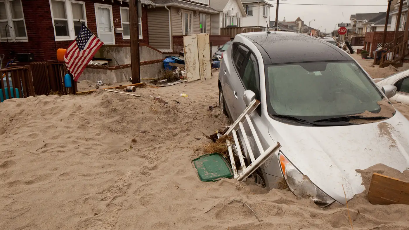Silver sedan half buried in sand and debris on a residential street in Long Island after Hurricane Sandy