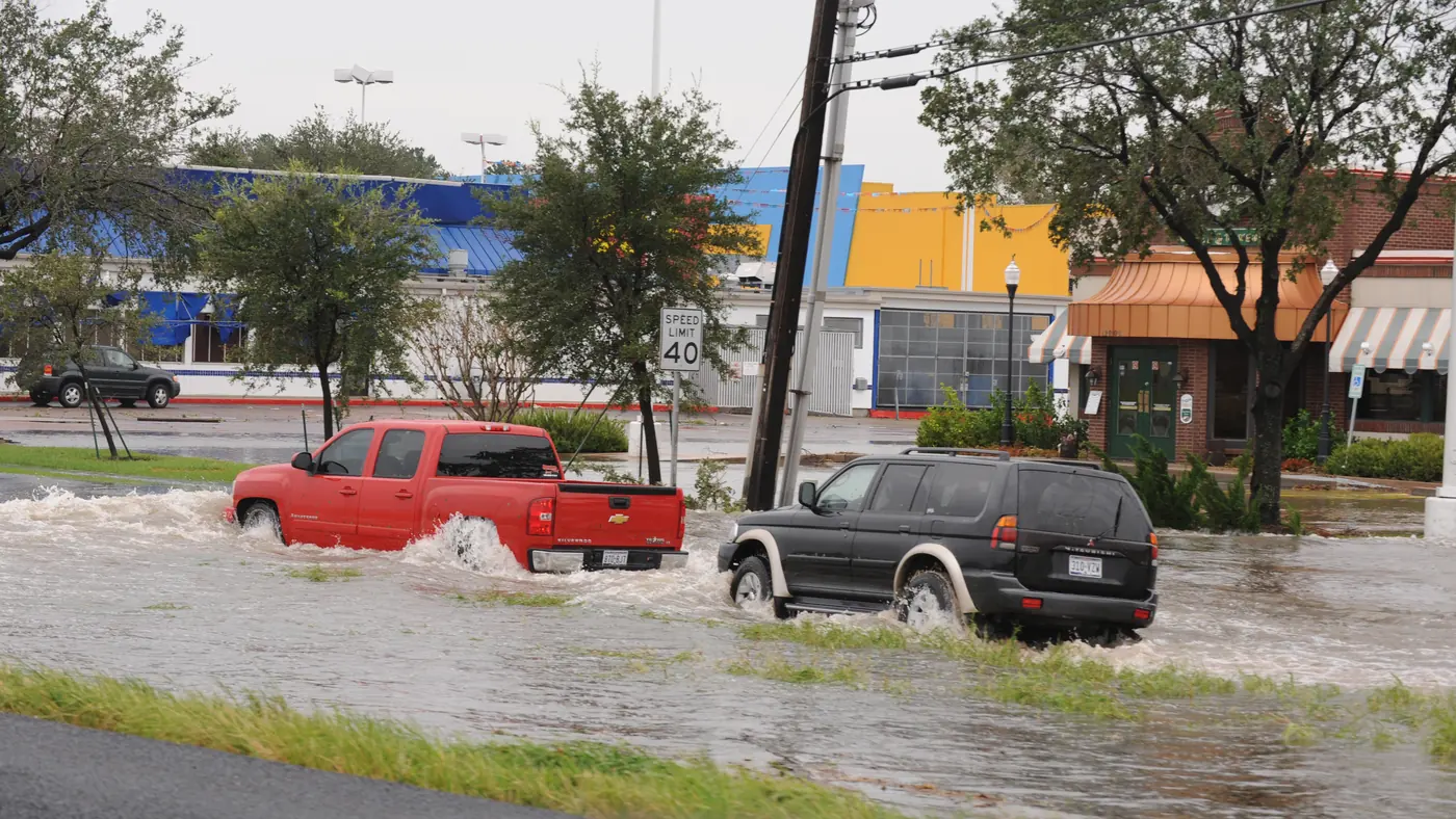 A red pickup and a dark SUV driving through deep flood water on a city street in Houston after Hurricane Ike