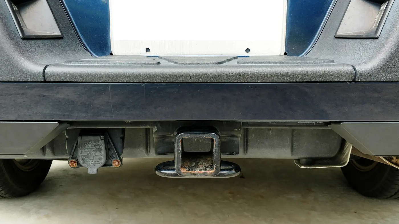 Class III square receiver hitch under a pickup’s rear bumper, with a 7-pin trailer wiring socket mounted to its left