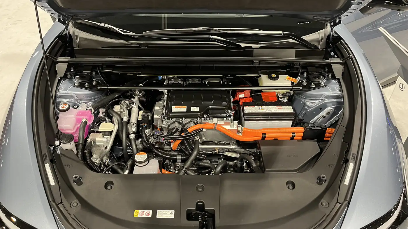 Front compartment of a Lexus RZ 450e electric SUV, hood open, showing orange high-voltage cables and the drive unit
