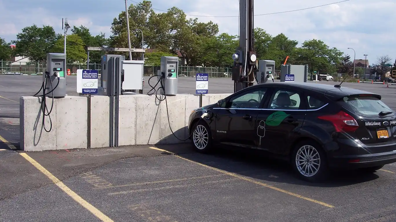 Black Ford Focus Electric hatchback plugged into one of a row of public charging stations in a parking lot