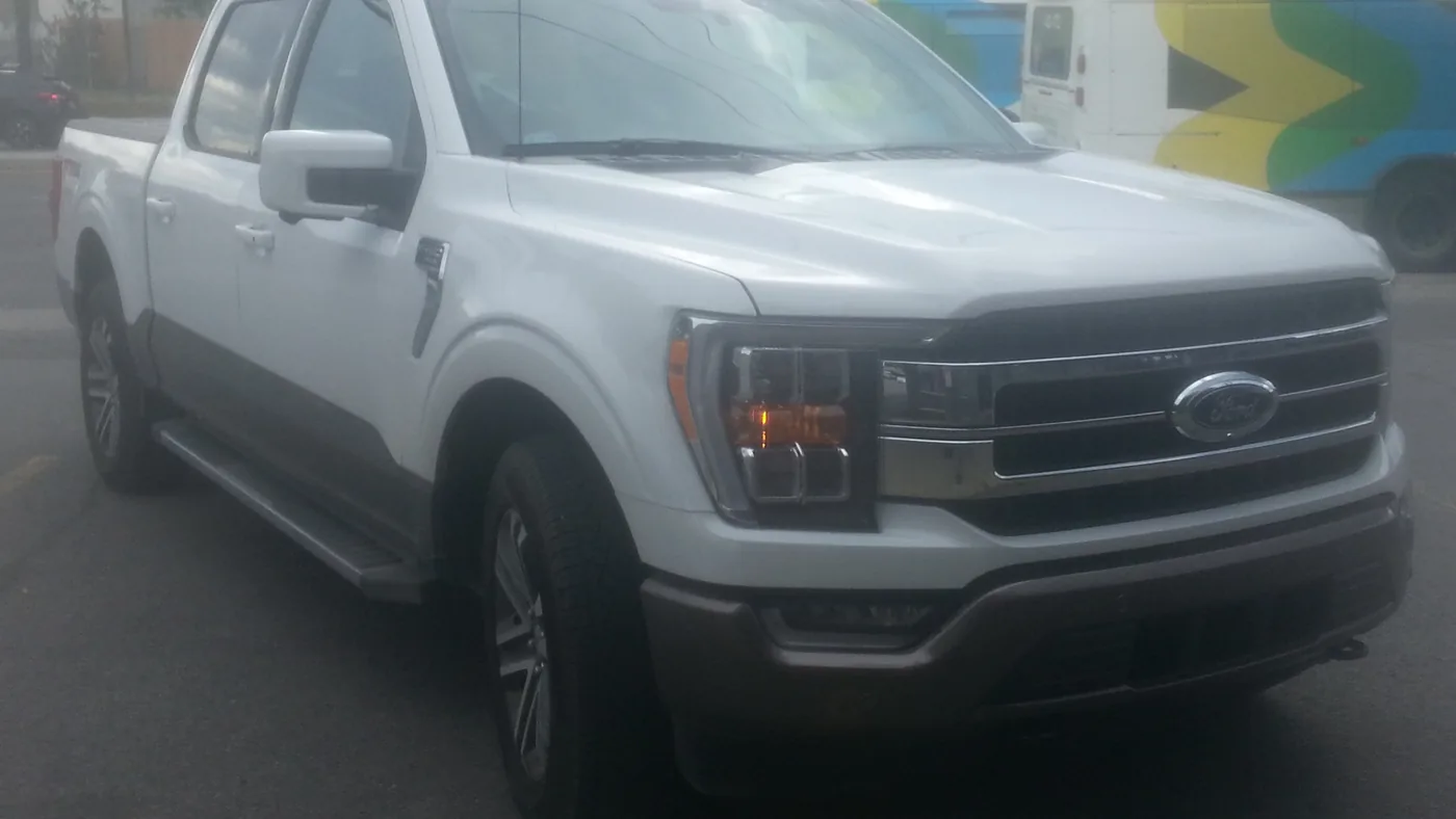 White 2021 Ford F-150 crew cab pickup seen from the front right, with the windshield wipers parked below the glass