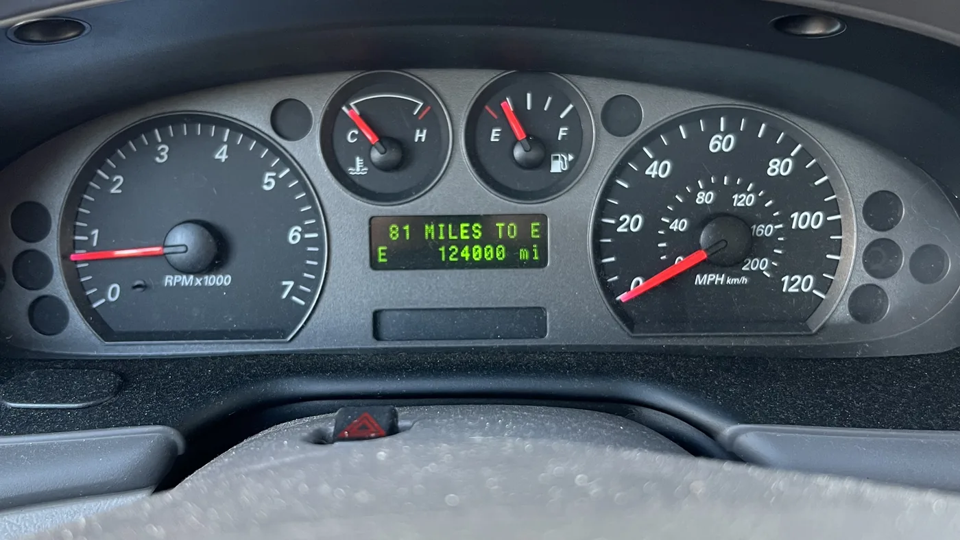 Analog instrument cluster with tachometer, speedometer, temperature and fuel gauges and a green text display showing mileage