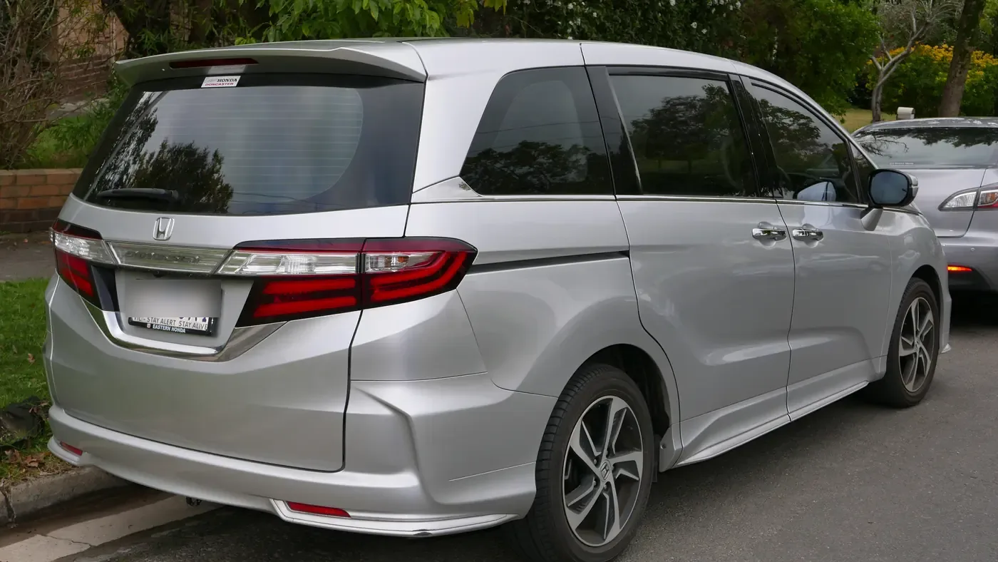 Silver Honda Odyssey minivan parked at a curb, seen from the rear right