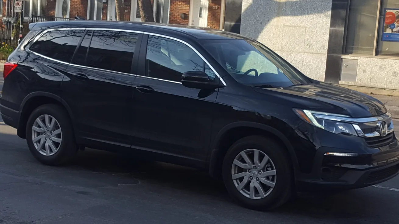 Black 2019 Honda Pilot SUV driving past a brick building, seen from the front right