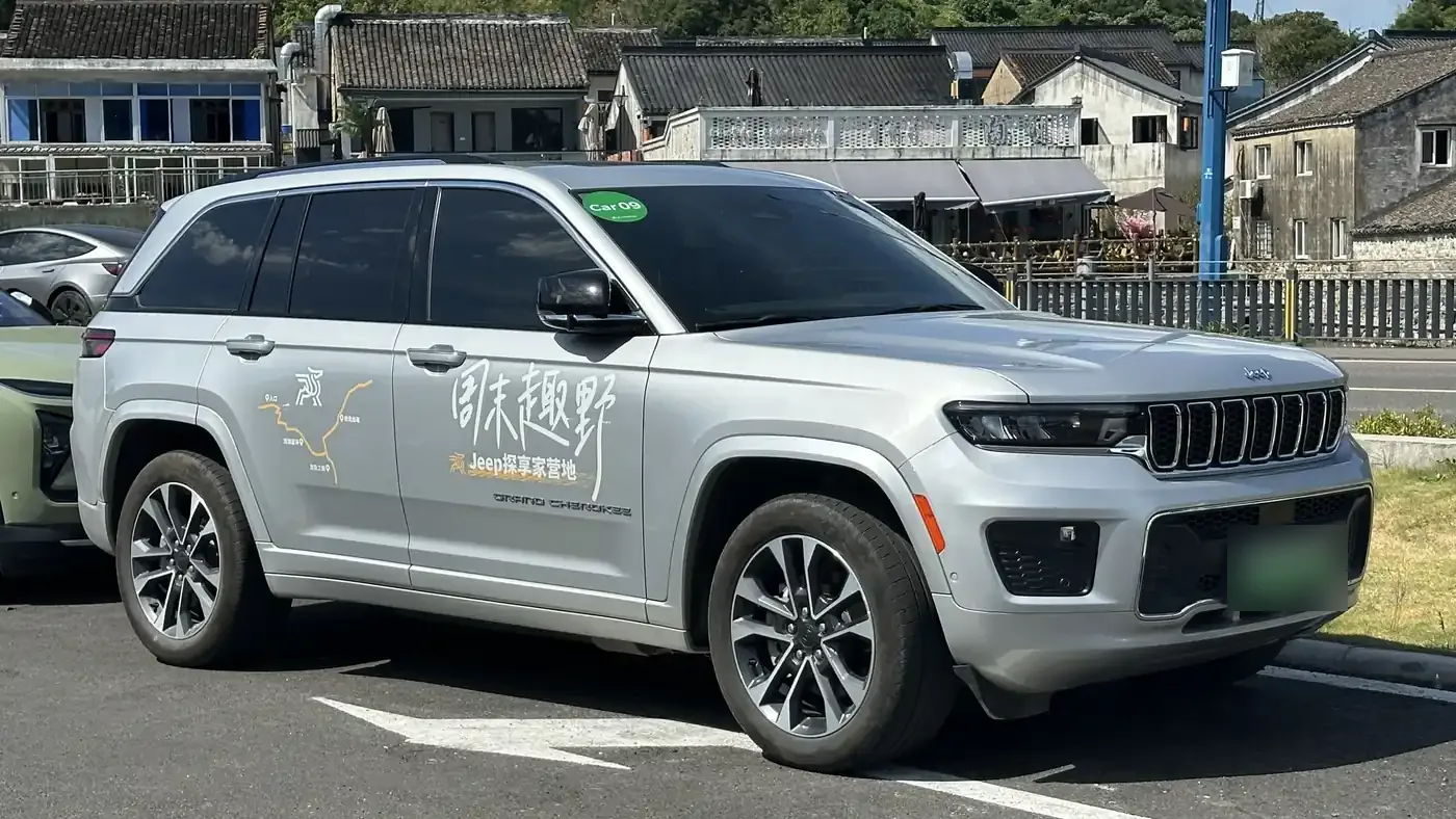 Silver Jeep Grand Cherokee 4xe SUV parked on asphalt, seen from the front right with its license plate blurred
