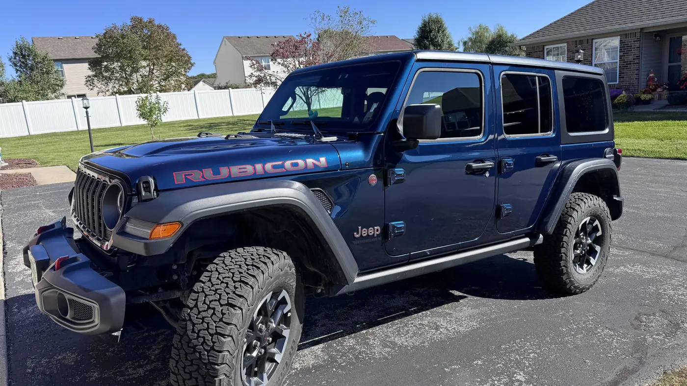 Dark blue Jeep Wrangler Rubicon four-door SUV with off-road tires parked on a suburban driveway