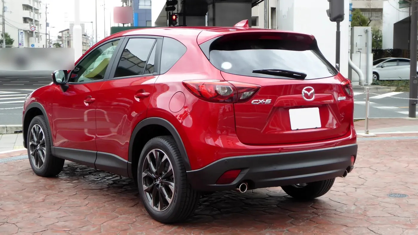 Red first-generation Mazda CX-5 SUV seen from the rear left, liftgate closed, parked on a paved plaza