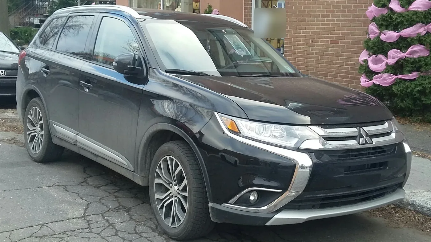 Black 2016 Mitsubishi Outlander SUV parked on a cracked lot beside a brick building, seen from the front right