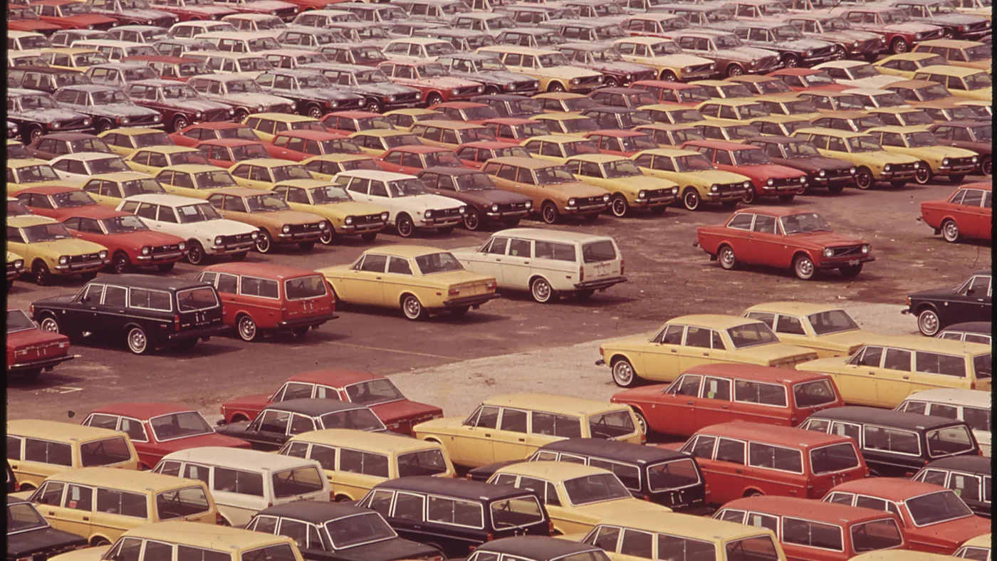 Hundreds of new cars and station wagons in red, yellow, white and black parked in tight rows at a port terminal