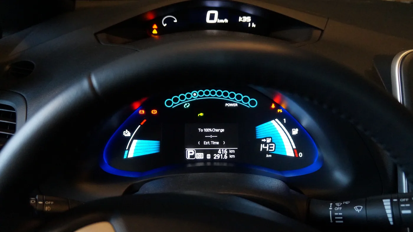 Illuminated instrument cluster of a 2013 Nissan Leaf with battery and range gauges behind the steering wheel