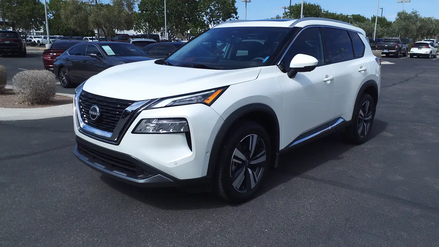 White 2023 Nissan Rogue SL compact SUV parked on a dealer lot on a sunny day