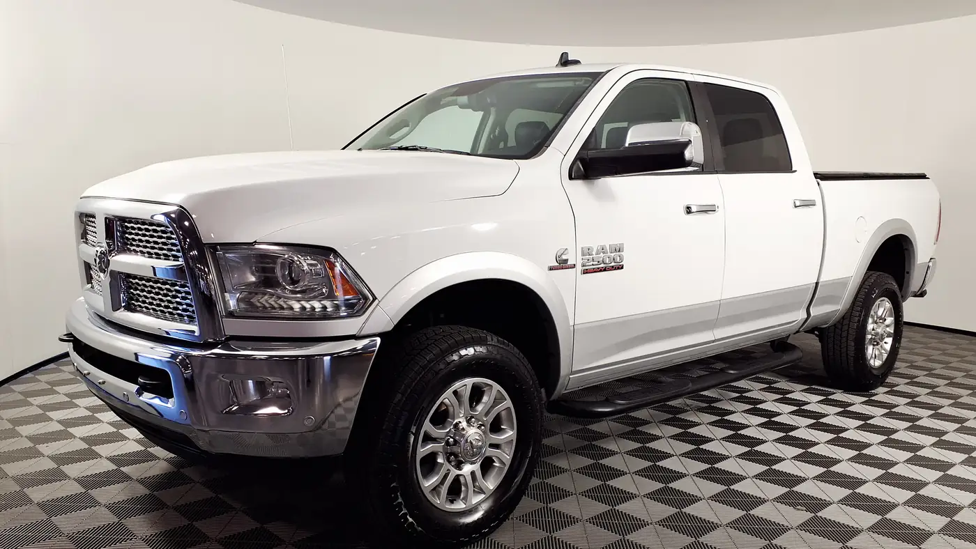 White 2016 Ram 2500 Laramie crew cab pickup with a Cummins diesel badge on the fender, in a showroom