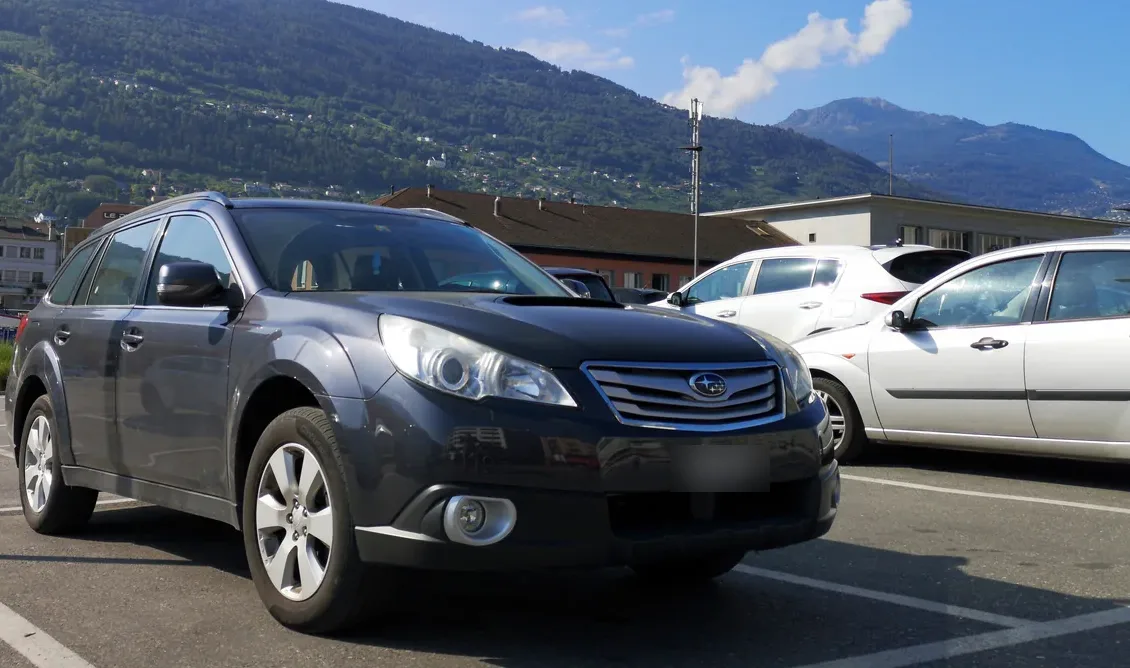 Dark gray Subaru Outback wagon parked in a lot in front of a mountain slope, seen from the front left