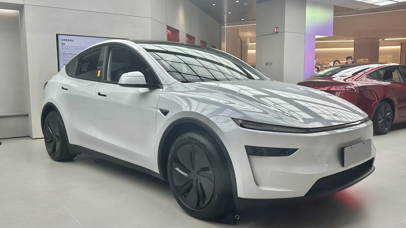 White Tesla Model Y electric SUV parked in a bright showroom, seen from the front three-quarter angle
