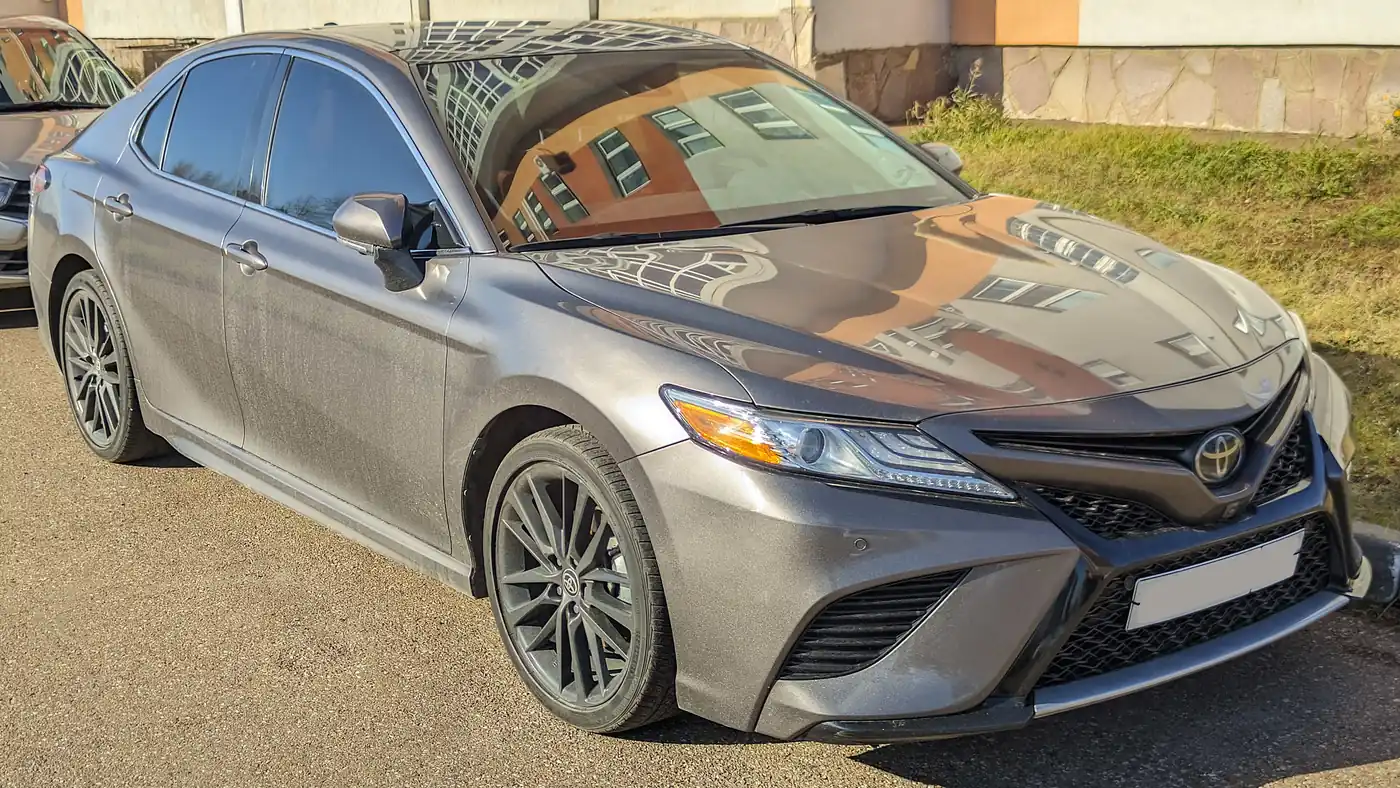 Grey Toyota Camry XSE sedan parked on asphalt beside a grassy bank, seen from the front right