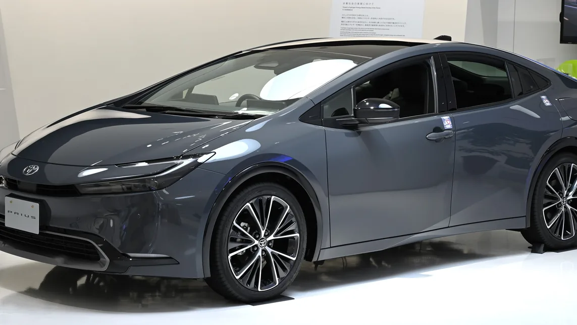 Dark gray 2023 Toyota Prius Z hybrid hatchback on show in a showroom with a white floor, seen from the front left
