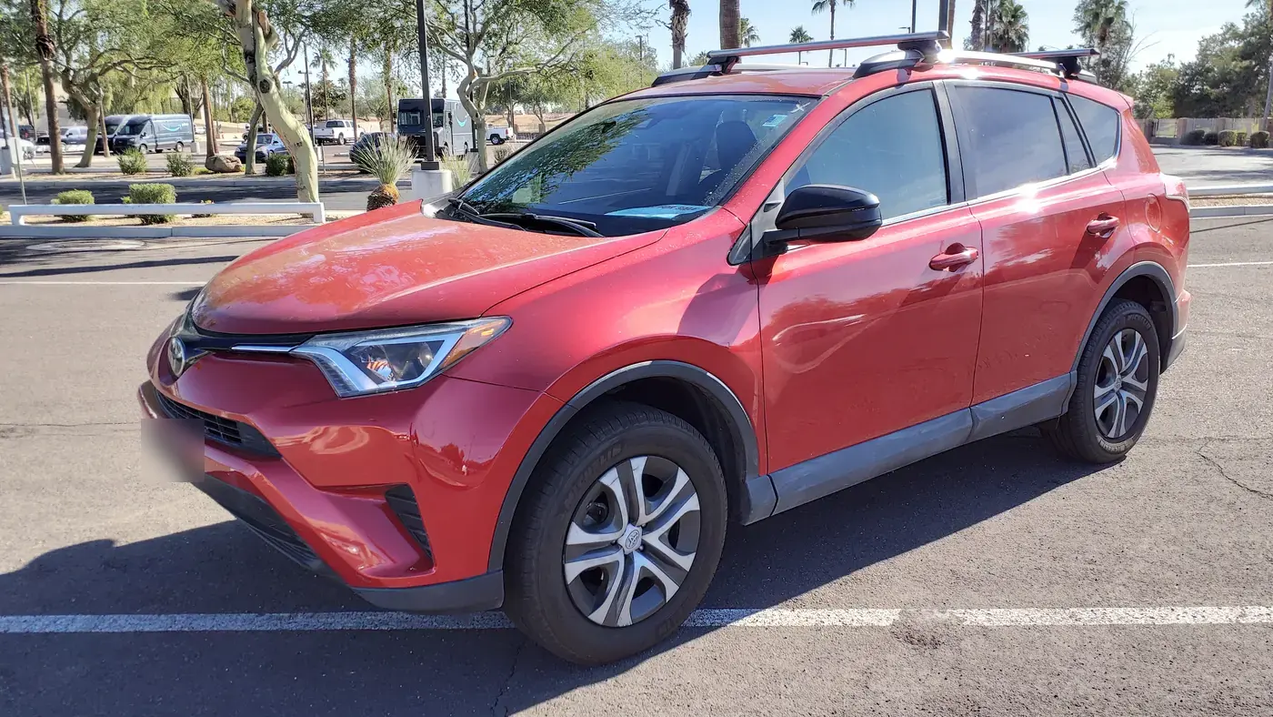 Red 2017 Toyota RAV4 LE with roof rails parked in a lot, seen from the front left